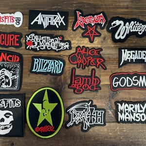 May include: A collection of embroidered patches featuring various band logos and symbols. The patches are in various shapes and sizes, with bold colors and detailed designs. Bands include Misfits, Anthrax, and Megadeth.