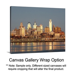 May include: A panoramic view of a city skyline at dusk. The city is lit up with lights, and the buildings are reflected in the water. The sky is a soft blue, and the water is a dark blue. The image is a sample for a canvas gallery wrap option.
