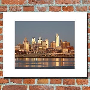 May include: A panoramic view of the Philadelphia skyline at sunset, with the city's iconic skyscrapers reflected in the water.