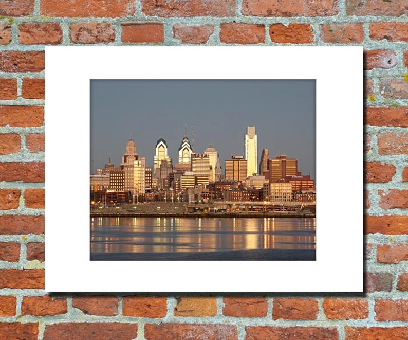 May include: A panoramic view of the Philadelphia skyline at sunset, with the city's iconic skyscrapers reflected in the water.
