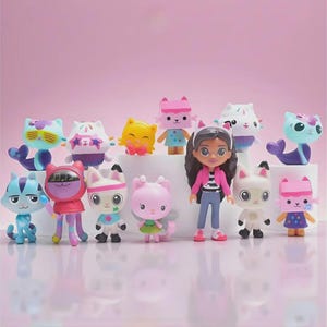Puede incluir: Una colección de figuras coloridas de Gabby's Dollhouse, que incluyen personajes con temas de gatos y una muñeca. Las figuras están en varias poses y atuendos, con un fondo rosa. Los personajes son de varios colores, incluyendo azul, rosa, amarillo y blanco.