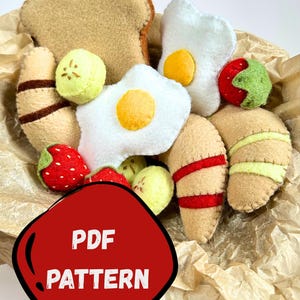 May include: A felt breakfast set includes a slice of toast, fried eggs, croissants, strawberries, and kiwi slices. The set is displayed in a paper-lined container. Text on the image reads "FELT BREAKFAST SET" and "PDF PATTERN".