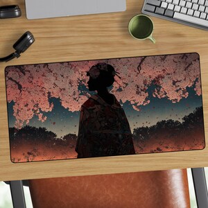 Puede incluir: Alfombrilla de escritorio rectangular con la silueta de una mujer con kimono bajo un cerezo en flor. La alfombrilla tiene un borde negro y una colorida ilustración con tonos rosas, naranjas y azules.