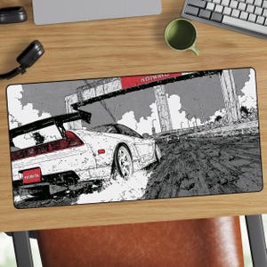 May include: A rectangular mousepad featuring a white sports car drifting on a muddy road, with a black and white manga-style illustration. The car has a large rear wing and red taillights. The word "HONDA" is visible.