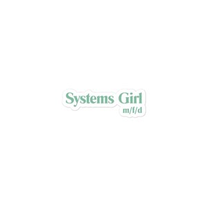 May include: A white sticker with the text "Systems Girl" in a light green color. Below the text is "m/f/d" in a smaller font. The sticker has a white border and is set against a white background.