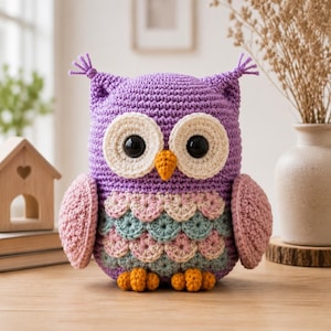 Può includere: Un peluche a forma di gufo realizzato all'uncinetto con corpo viola, grandi occhi neri con toppe circolari color crema e un piccolo becco arancione. Il petto presenta un motivo a squame con file alternate di filato rosa chiaro e azzurro.