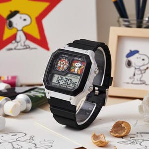 May include: A digital watch with a black strap and a silver-coloured frame. The watch face displays Snoopy graphics and the time. The background includes Snoopy artwork and a drawing of Snoopy wearing a beret.