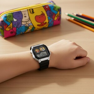 May include: A black and white digital watch with a black band is worn on a wrist. The watch face displays cartoon characters and the time. A colorful pencil case and colored pencils are in the background.