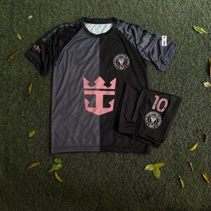 May include: A short-sleeve athletic shirt and matching shorts set in black and dark gray. The shirt features a large pink crown logo, the Inter Miami CF crest, and the text "cht" on the sleeve. The shorts display the number 10 and the team crest.