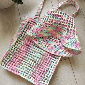 Peut inclure: Un sac fourre-tout et un chapeau de soleil assortis en crochet, aux couleurs pastel rose, bleu, jaune et blanc. Le motif ajouré est visible, et le sac a deux anses. Le chapeau a un large bord.