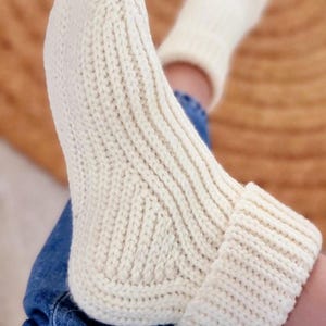 Peut inclure: Gros plan sur une paire de chaussettes tricotées de couleur crème. Les chaussettes ont un motif côtelé sur la jambe et un revers plié. Les chaussettes sont portées avec un jean bleu.
