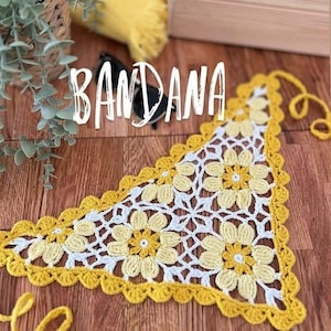 Peut inclure: Bandana triangulaire faite à la main avec un motif floral au crochet. La base est blanche avec des fleurs jaunes et une bordure festonnée jaune. Le mot "BANDANA" est écrit en blanc en haut.