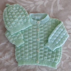 Peut inclure: Ensemble pour bébé en tricot vert menthe, comprenant un cardigan à boutons et un bonnet assorti. L'ensemble présente un motif texturé et tissé. Le cardigan a des manches longues et un col rond. Le chapeau a un petit pompon sur le dessus.