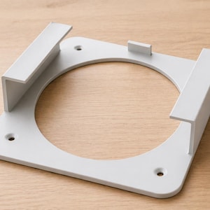 Op de afbeelding: Een witte, vierkante beugel met een cirkelvormige opening in het midden. De beugel heeft twee L-vormige armen en een klein rechthoekig stuk. Er zijn drie gaten zichtbaar. De beugel is van metaal.