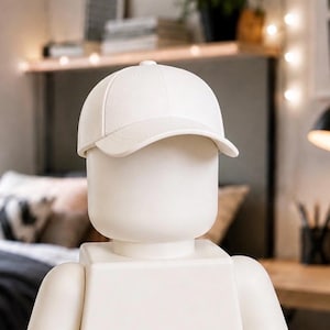 Peut inclure: Une casquette de baseball blanche unie avec une visière incurvée, portée sur la tête d'une figurine en plastique blanc lisse et sans traits. La casquette présente une construction classique à six panneaux avec un bouton au sommet.