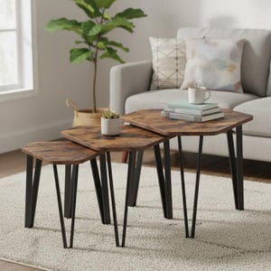 Op de afbeelding: Set van drie nesttafels met zeshoekige bladen en zwarte haarspeldpoten. De tafelbladen hebben een distressed houtlook afwerking. De grootste tafel is ongeveer 61 cm breed, 61 cm diep en 51 cm hoog.