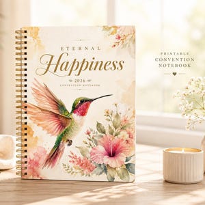 Könnte beinhalten: Ein Spiralnotizbuch mit den Worten "Eternal Happiness 2026" und einer Kolibri-Illustration. Das Cover zeigt Aquarellblumen und einen Kolibri mit roten, grünen und rosa Federn. Das Notizbuch liegt auf einer Holzoberfläche mit einer Kerze und einer Vase.