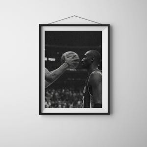 Può includere: Stampa incorniciata in bianco e nero con un giocatore di basket. Il giocatore guarda una palla da basket che gli viene offerta. Il testo "lock in" è stampato sull'immagine.