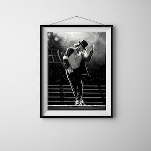 Puede incluir: Impresión enmarcada en blanco y negro de un artista en el escenario, con sombrero negro, chaqueta y pantalón. El artista es capturado a mitad de baile, con un brazo levantado y el otro a su lado. El fondo está borroso, con luces de escenario y un efecto brumoso.