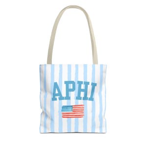 Könnte beinhalten: Eine Tragetasche mit hellblauem und weißem Streifenmuster. Die Tasche zeigt den blauen Text "APHI" und eine kleine amerikanische Flagge. Sie hat einen beigefarbenen Griff.