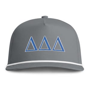 Könnte beinhalten: Eine graue Baseballkappe mit drei gestickten blauen griechischen Delta-Symbolen, die horizontal auf der Vorderseite angeordnet sind. Die Kappe verfügt über eine weiße Kordel entlang der Basis der Krone, direkt über dem flachen Schirm.