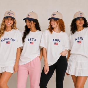 Könnte beinhalten: Vier Personen tragen passende Outfits: weiße T-Shirts mit griechischen Buchstaben und einem amerikanischen Flaggenmuster, kombiniert mit khakifarbenen Baseballkappen mit marineblauen Krempen. Die Outfits werden durch verschiedene Unterteile ergänzt, darunter Shorts, eine rosa Hose und schwarze Leggings.