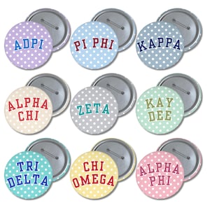 May include: A collection of nine circular pin-back buttons featuring white polka dots on various pastel backgrounds. Each button displays a Greek organization name in bold, block lettering, including ADPI, PI PHI, KAPPA, ALPHA CHI, ZETA, KAY DEE, TRI DELTA, CHI OMEGA, and ALPHA PHI.