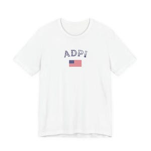 Könnte beinhalten: Weißes T-Shirt mit dem blauen Schriftzug "ADPI" und einem kleinen amerikanischen Flaggen-Design. Das T-Shirt hat einen Rundhalsausschnitt und ist für den täglichen Gebrauch geeignet.