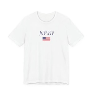 Könnte beinhalten: Weißes T-Shirt mit dem blauen Text "APHI" und einem amerikanischen Flaggen-Design. Das T-Shirt hat einen Rundhalsausschnitt. Ein einfaches, lässiges Oberteil.