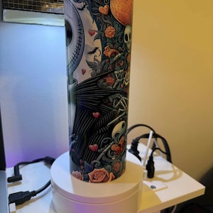 Puede incluir: Un vaso cil&iacute;ndrico de acero inoxidable con un dise&ntilde;o de Jack Skellington de Pesadilla antes de Navidad. El dise&ntilde;o incluye rosas, corazones y una calavera. El vaso mide unos 25 cm de alto y tiene una tapa plateada.