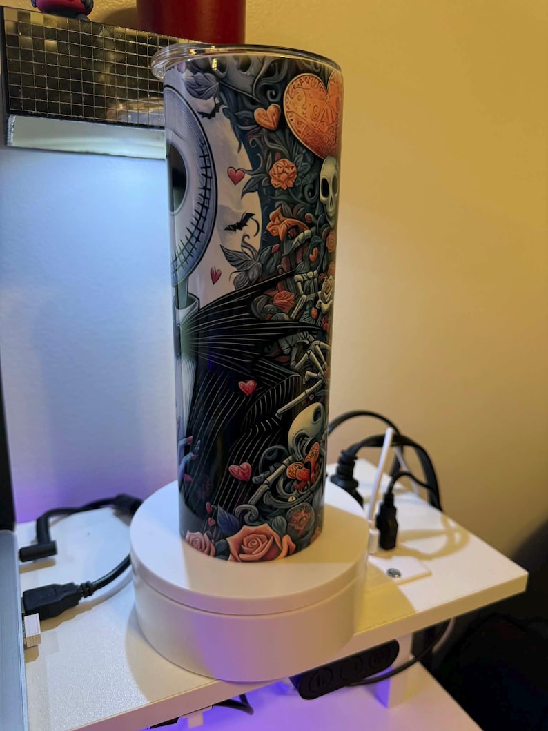 Puede incluir: Un vaso cil&iacute;ndrico de acero inoxidable con un dise&ntilde;o de Jack Skellington de Pesadilla antes de Navidad. El dise&ntilde;o incluye rosas, corazones y una calavera. El vaso mide unos 25 cm de alto y tiene una tapa plateada.