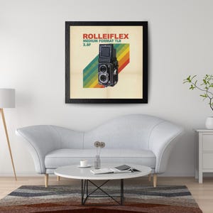 May include: A framed print featuring a vintage Rolleiflex medium format TLR camera. The print has a cream-colored background with a diagonal rainbow stripe design. The text "ROLLEIFLEX MEDIUM FORMAT TLR 2.8F" is displayed in red and green.