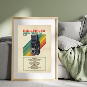 May include: Framed print featuring a vintage RolleiFlex Medium Format TLR 2.8F camera. The poster has a retro design with a rainbow stripe and text. The camera is black and silver, with detailed features.