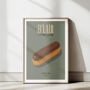 May include: A framed wall art print featuring a centred illustration of a chocolate-glazed eclair on a muted sage green background. The text ECLAIR is printed in large cream letters at the top, with LA PATISSERIE FRANCAISE and DEPUIS 1988 PARIS below.
