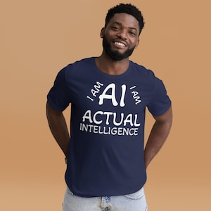 Puede incluir: Una camiseta azul marino con el texto blanco "I AM AI ACTUAL INTELLIGENCE". La camiseta es de manga corta y tiene cuello redondo. La persona que lleva la camiseta está sonriendo.