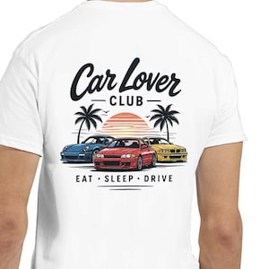 Könnte beinhalten: Weißes T-Shirt mit einer Grafik von drei Autos, Palmen und einem Sonnenuntergang. Der Text "Car Lover Club" steht über den Autos und "EAT • SLEEP • DRIVE" darunter. Die Autos sind blau, rot und gelb.