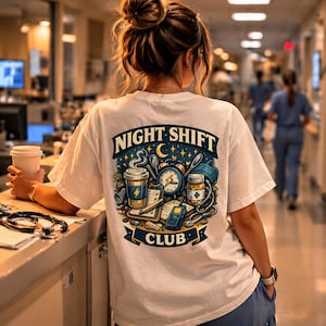 Peut inclure: T-shirt blanc avec un motif coloré dans le dos, indiquant "NIGHT SHIFT CLUB". Le design comprend une tasse de café, une horloge, un flacon de médicaments et un stéthoscope. La personne porte le t-shirt dans un cadre hospitalier.