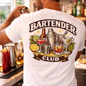 Peut inclure: T-shirt blanc avec un motif "BARTENDER CLUB". Le motif présente des verres à cocktails, un shaker et des tranches de fruits. Le t-shirt est porté par une personne dans un bar.
