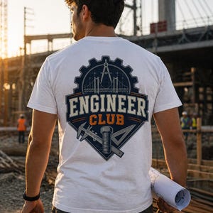 Könnte beinhalten: Weißes T-Shirt mit einem marineblauen und orangefarbenen Engineer Club-Logo auf dem Rücken. Das Logo zeigt ein Zahnrad, eine Brücke und technische Werkzeuge. Das T-Shirt ist kurzärmlig. Eine Person hält eine gerollte Bauzeichnung und einen weißen Helm.