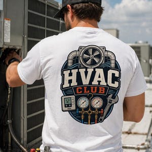 May include: White t-shirt with a graphic on the back featuring the text "HVAC CLUB" in a stylized design. The design includes a fan, gauges, and a wrench, suggesting an HVAC theme. The shirt is worn by a person working on an air conditioning unit.