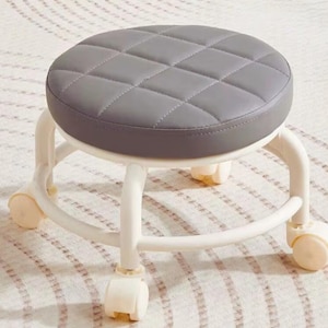 May include: A gray, round stool with a quilted seat and a white frame. The stool has four wheels for easy movement. The seat is approximately 14 inches in diameter.