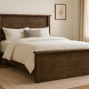 May include: A dark brown wooden bed frame with a matching headboard. The bed is made up with white bedding and pillows. A small side table with a lamp is on the left. The bed is on a beige rug.