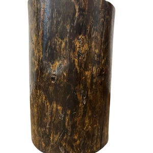Puede incluir: Un taburete o pedestal cil&iacute;ndrico de madera con un acabado marr&oacute;n oscuro, que muestra patrones de vetas naturales, nudos y una superficie texturizada. El objeto tiene una parte superior plana y un aspecto vertical ligeramente desgastado.