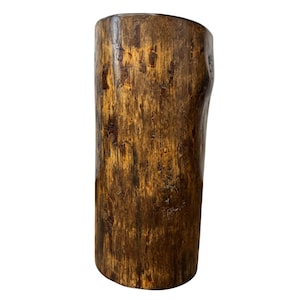 Puede incluir: Un pedestal cil&iacute;ndrico de madera con un acabado pulido, que muestra un patr&oacute;n de grano marr&oacute;n natural con vetas y nudos m&aacute;s oscuros en toda la superficie. La estructura presenta una parte superior plana y una orientaci&oacute;n vertical.