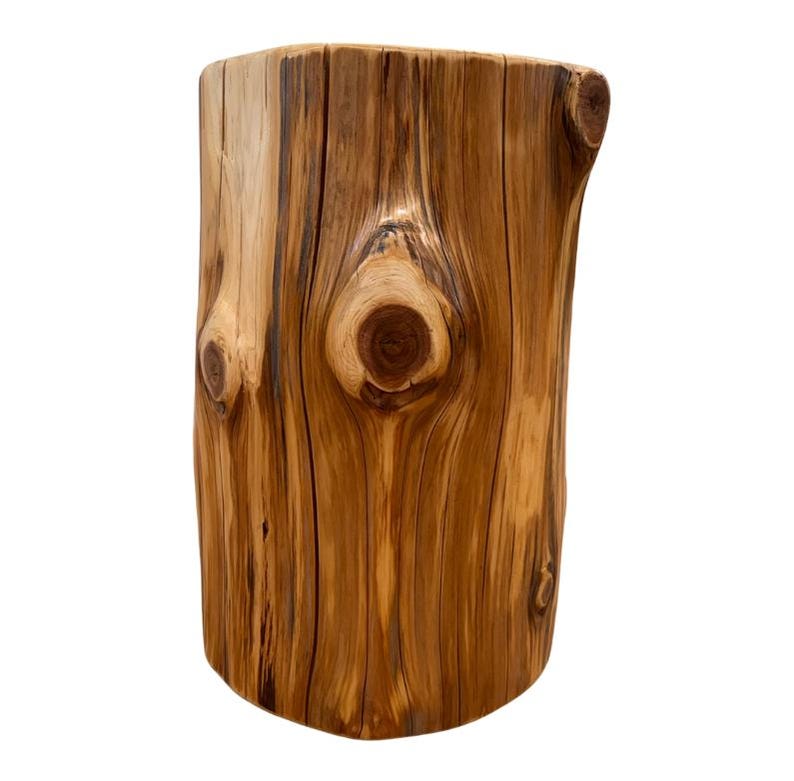 Pu&ograve; includere: Uno sgabello o tavolino cilindrico in legno ricavato da un unico tronco. La superficie presenta una finitura lucida color marrone chiaro e medio con venature naturali, fessure verticali e diversi nodi circolari di colore scuro.