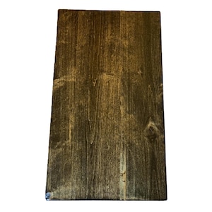 May include: A rectangular wooden board with a dark brown stain. The wood grain is visible, with lighter streaks and knots adding texture. The board is likely for crafting or home decor.