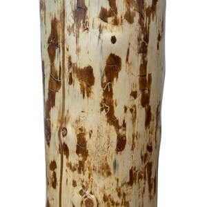 Puede incluir: Un taburete cil&iacute;ndrico de madera con una superficie lisa de color crema claro que presenta restos naturales de corteza marr&oacute;n oscuro, patrones intrincados de veta de madera y nudos visibles, en posici&oacute;n vertical.