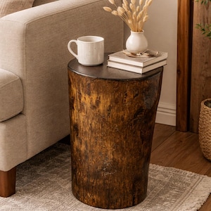 Puede incluir: Una mesa auxiliar cil&iacute;ndrica hecha de un toc&oacute;n de &aacute;rbol natural de color marr&oacute;n oscuro con una superficie superior plana y lisa. La mesa sostiene una taza de cer&aacute;mica blanca, un peque&ntilde;o jarr&oacute;n blanco con hierbas secas y dos libros apilados.