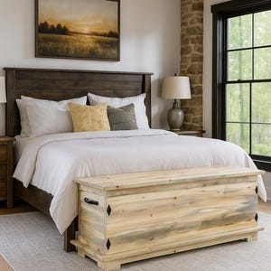 May include: A bedroom with a dark wooden bed, white bedding, and decorative pillows. A light wood chest is at the foot of the bed. A framed landscape painting hangs above the bed. The room has a rustic feel.