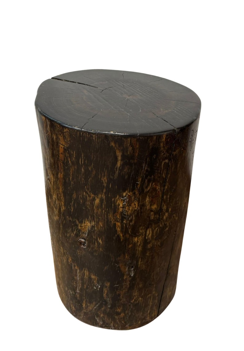 Puede incluir: Un taburete cil&iacute;ndrico de madera con un acabado oscuro te&ntilde;ido. La superficie superior muestra patrones de veta de madera natural y una grieta visible en el centro. Los lados presentan una apariencia rugosa y texturizada en tonos marrones.